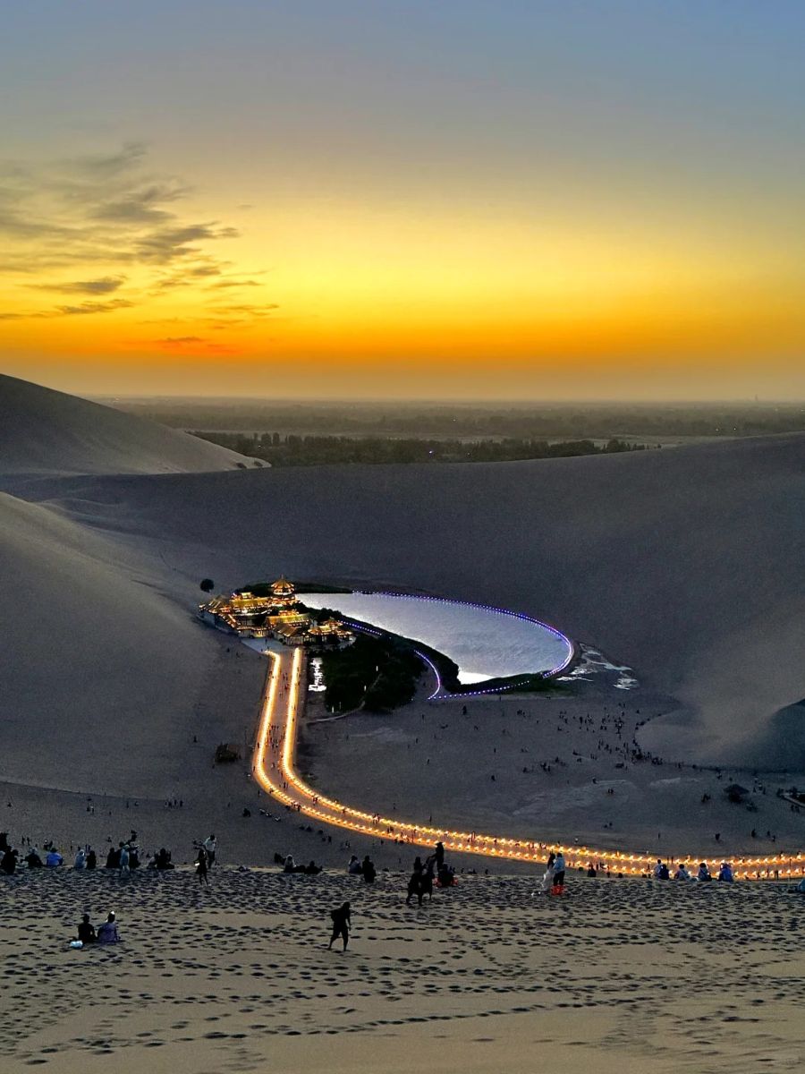 Stunning sunset over the vast Gobi Desert with illuminated attractions in the distance.