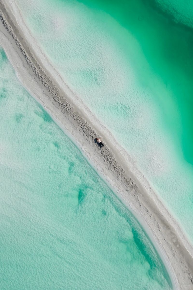 Aerial view of a sandy path surrounded by vibrant turquoise water.