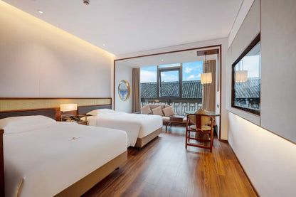 Stylish hotel room featuring two beds, wooden floors, and large windows with a scenic view.