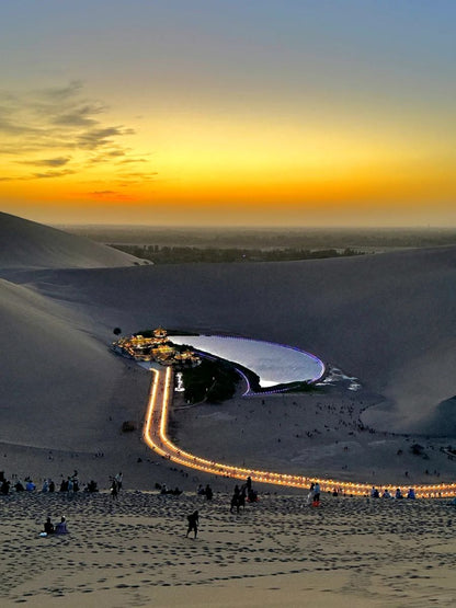 Stunning sunset over the vast Gobi Desert with illuminated attractions in the distance.
