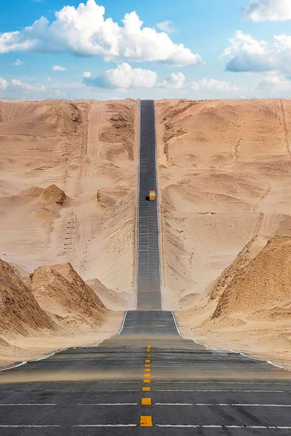 Desert road disappearing into the sandy landscape under a blue sky with clouds.